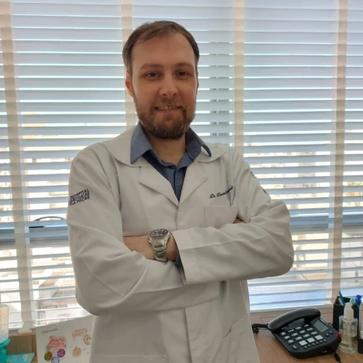 Dr. Lucas Müzell de jaleco, braços cruzados, no consultório