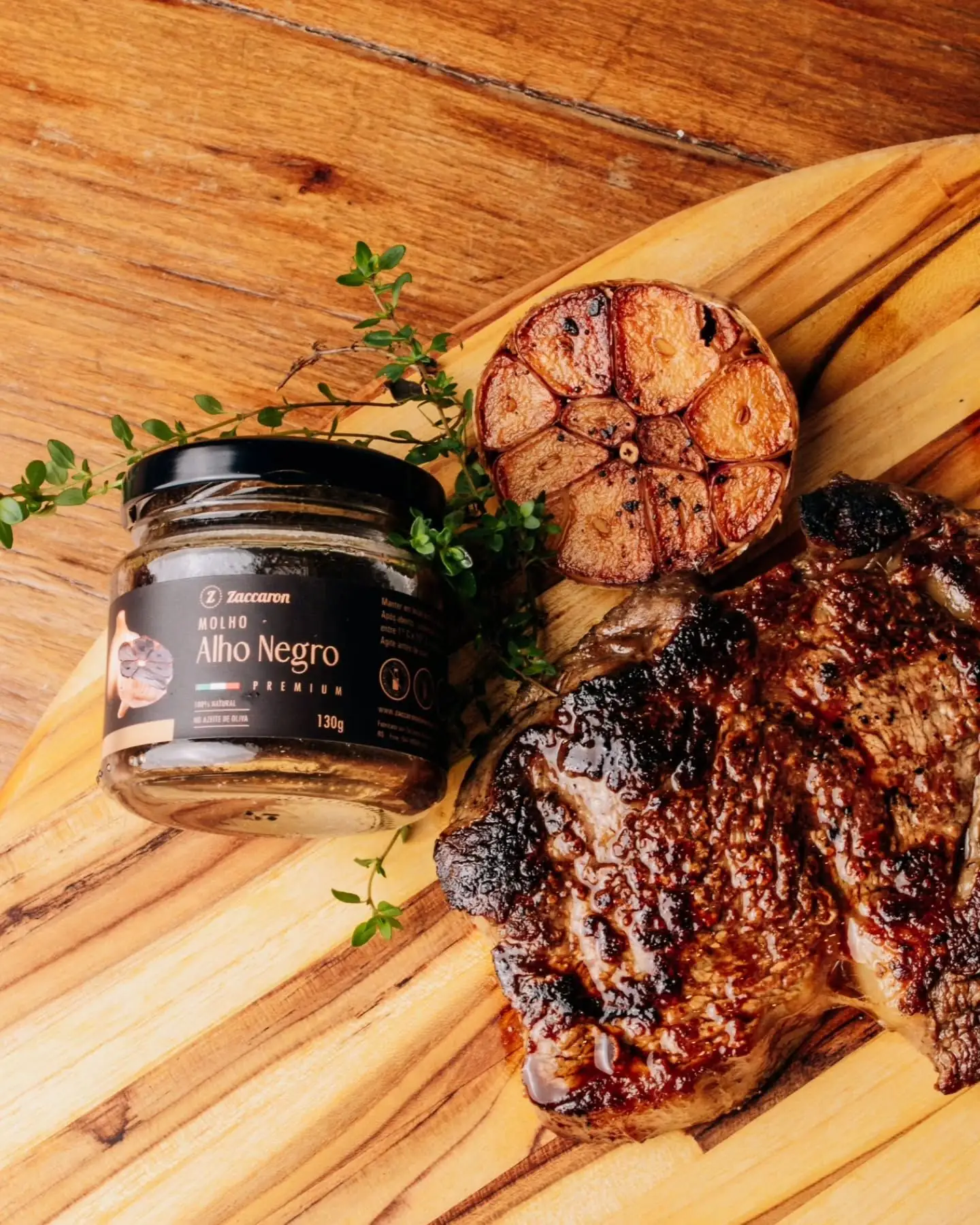 Pote de Molho de Alho Negro Zaccaron ao lado de carne grelhada e alho assado