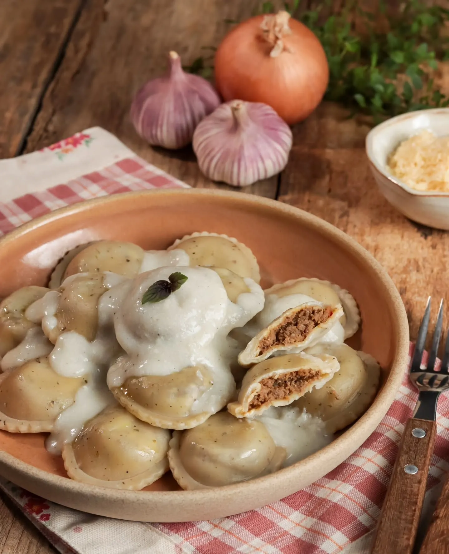 Prato de ravioli com molho branco servido sobre toalha xadrez vermelha