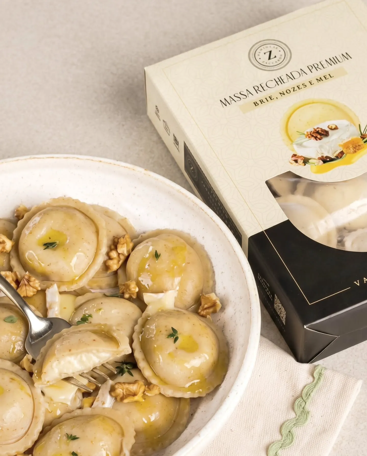 Massa recheada premium de brie, nozes e mel servida em prato branco ao lado da caixa